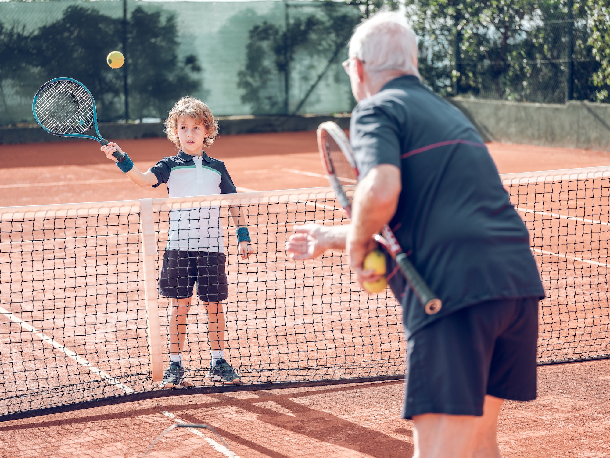Aged tennis player teaching cute kid on court